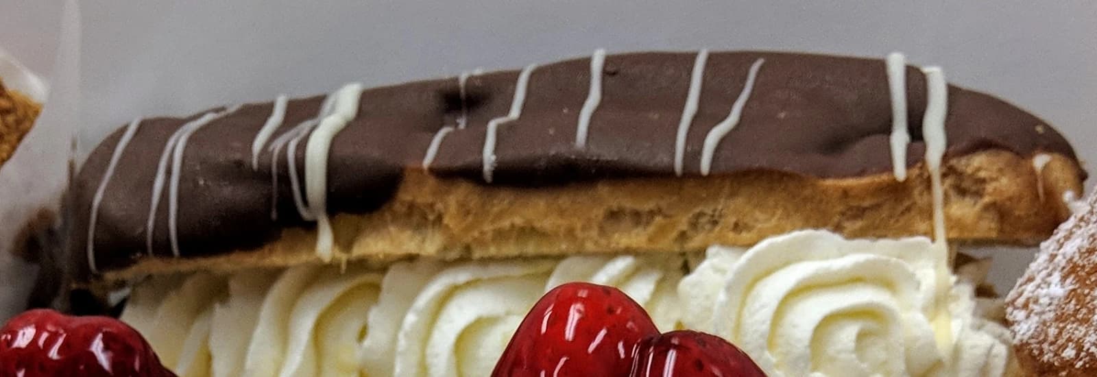 Close view of a chocolate-topped eclair filled with piped cream.