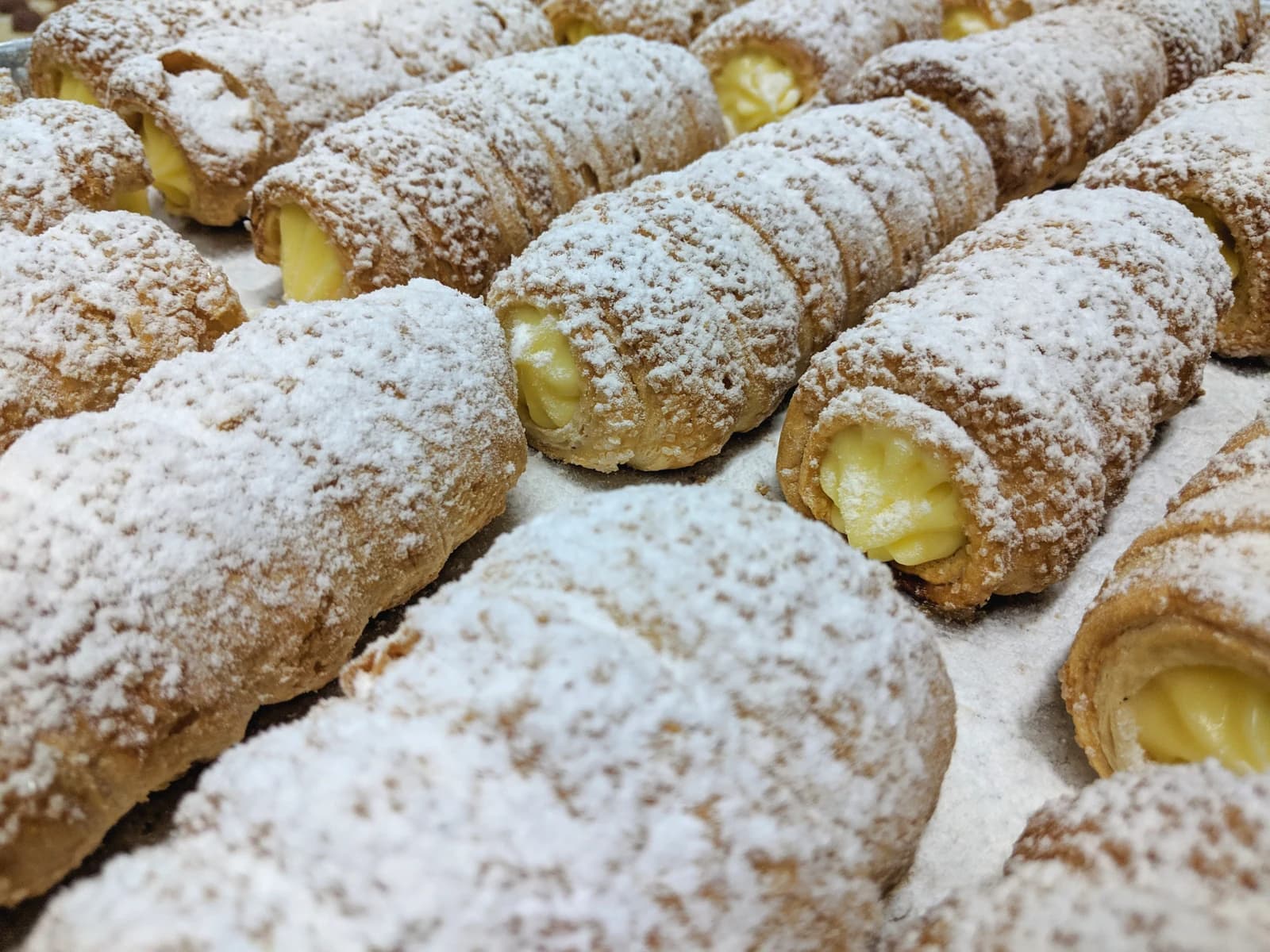 Custard-filled pastry horns dusted with icing sugar on a bakery tray.