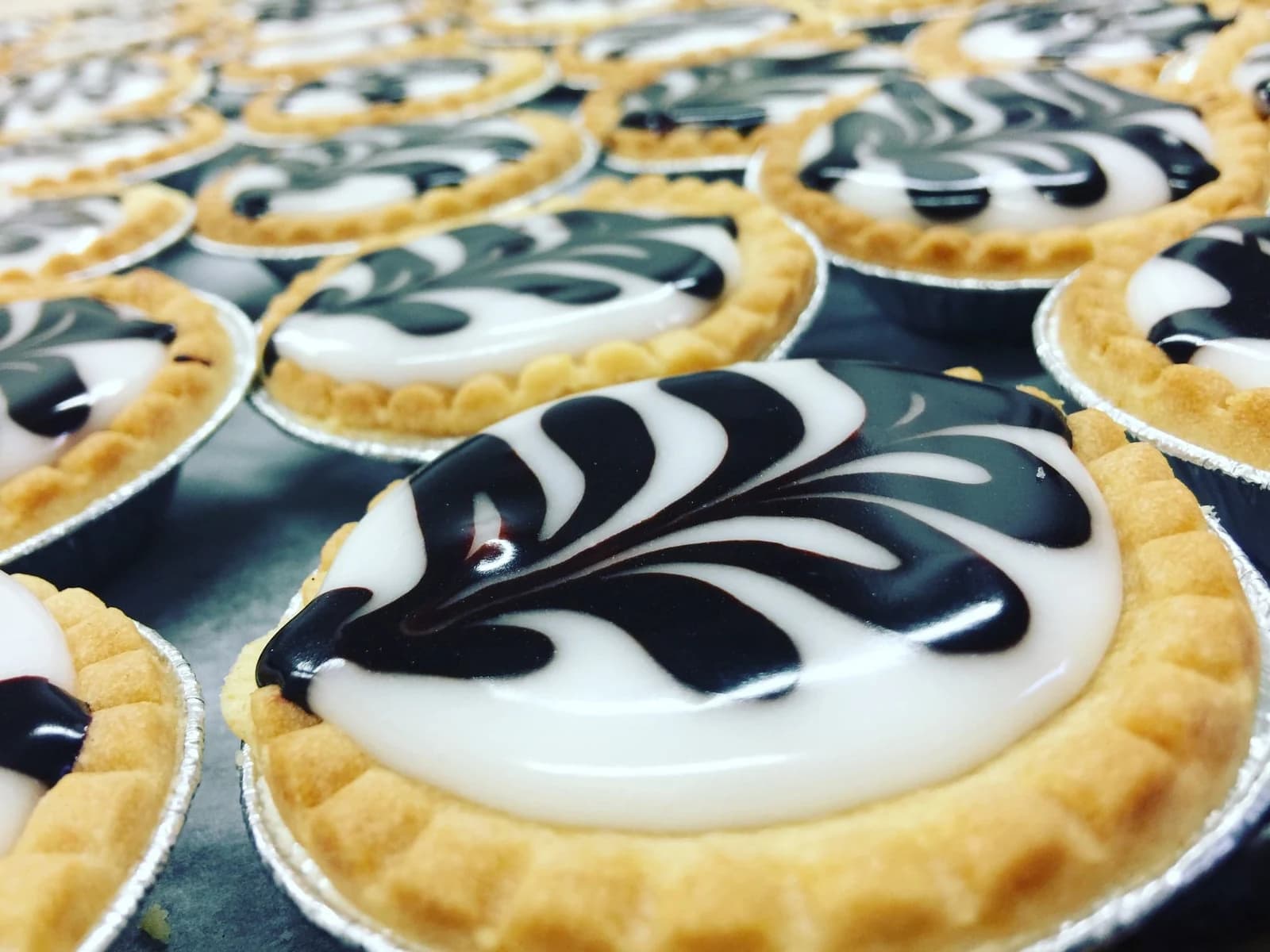 Fern tarts in foil cases with feathered chocolate and white icing.