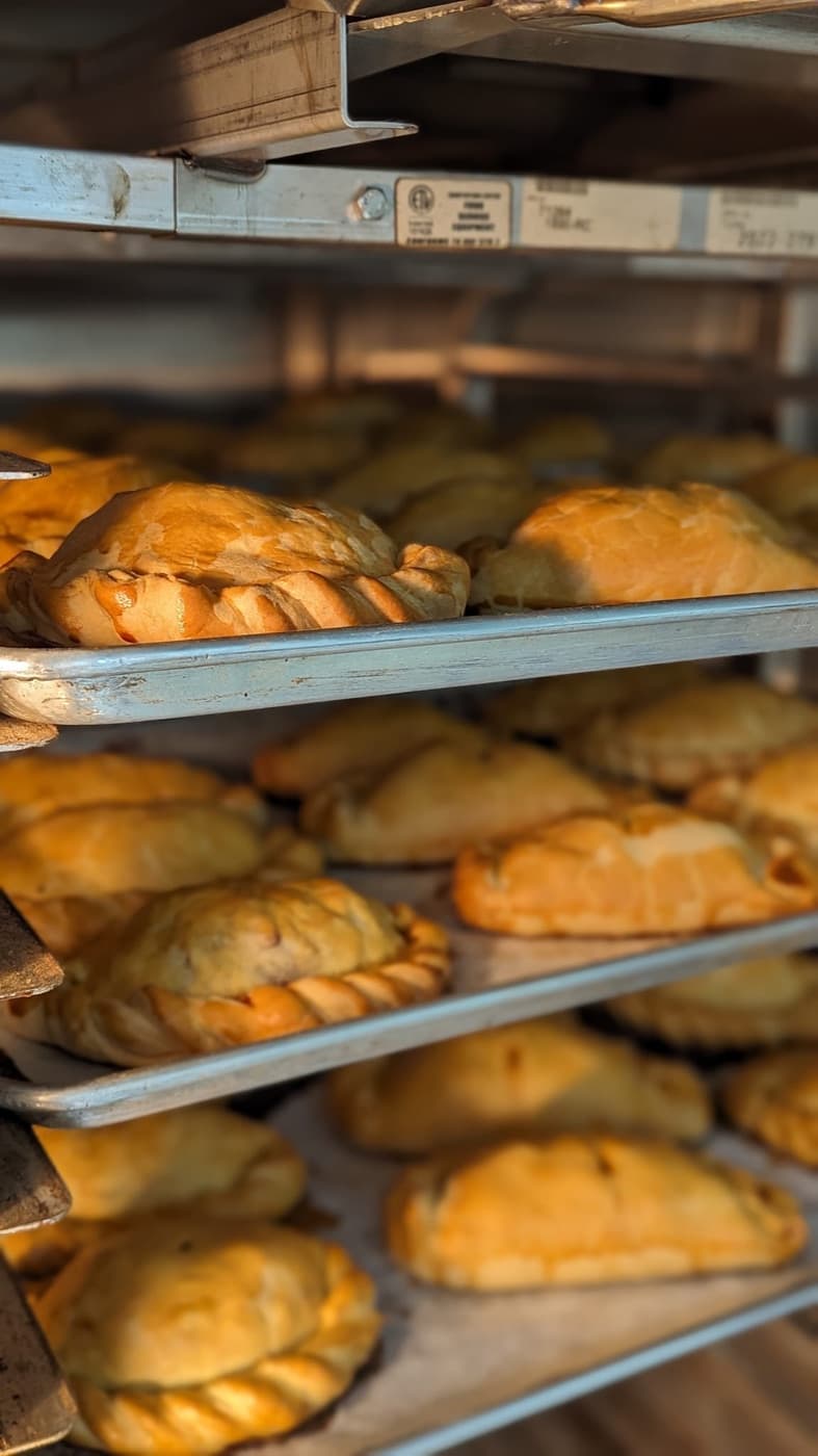 Rows of baked pasties on metal bakery trays.