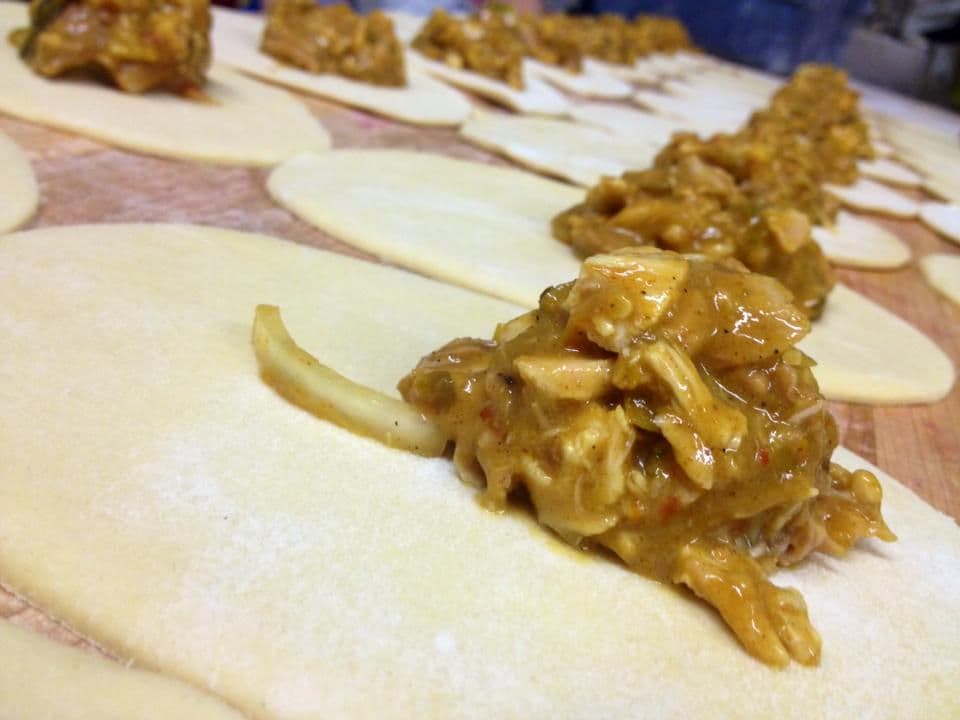 A golden puff pastry pasty filled with spiced chicken curry and diced vegetables, one end open.