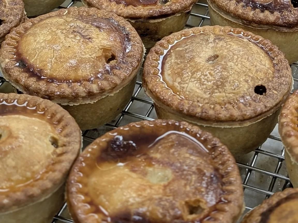 Glossy baked pork pies with crimped edges on a cooling rack.