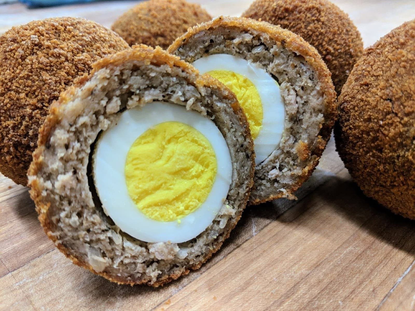 A golden breadcrumbed Scotch egg cut in half to show the pork layer wrapped around a whole boiled egg.