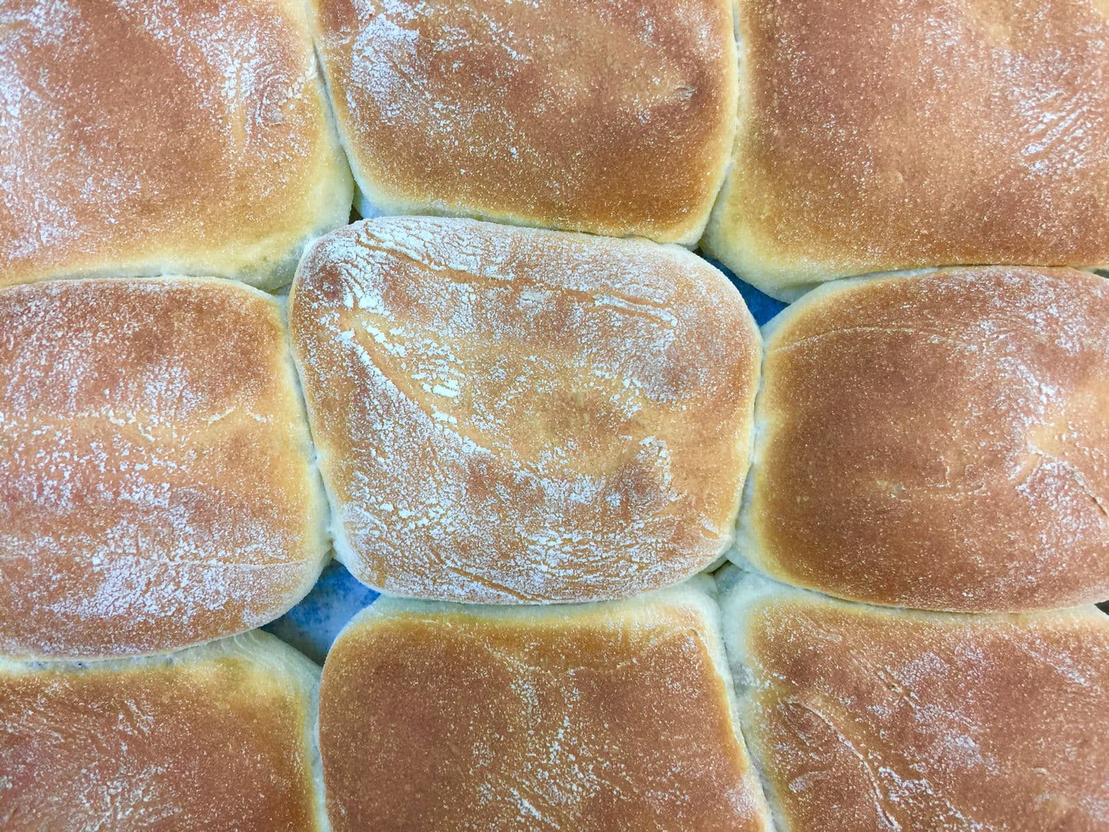 A cluster of soft floury Scottish morning rolls with pale golden tops, one split open ready to be filled