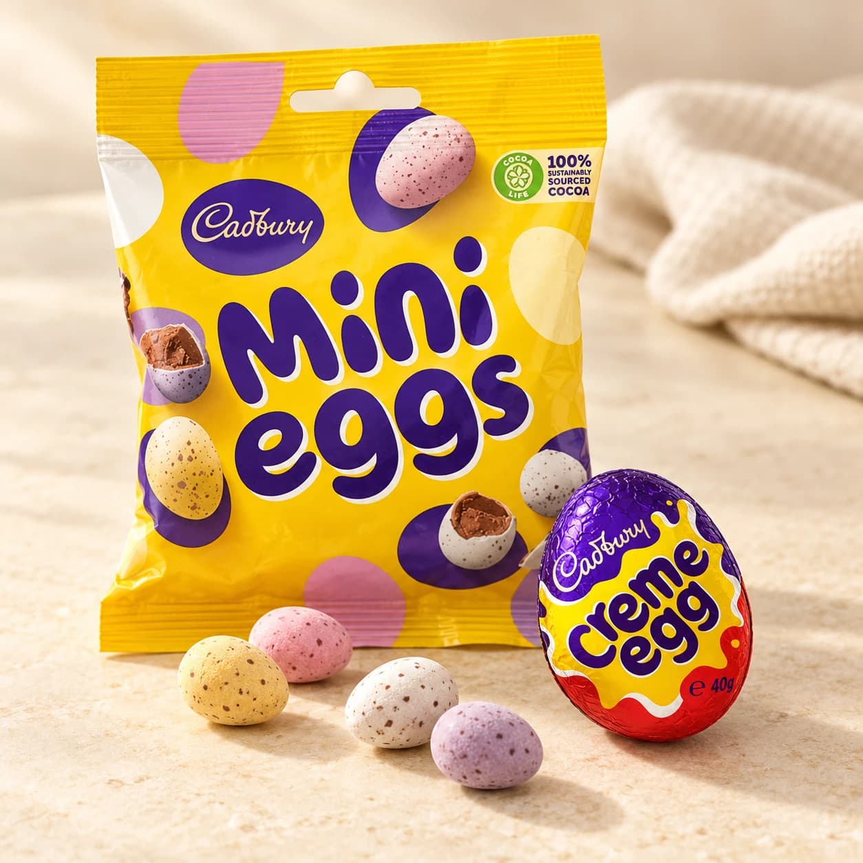 Cadbury Mini Eggs and Creme Eggs arranged on a pale surface with loose chocolate eggs.