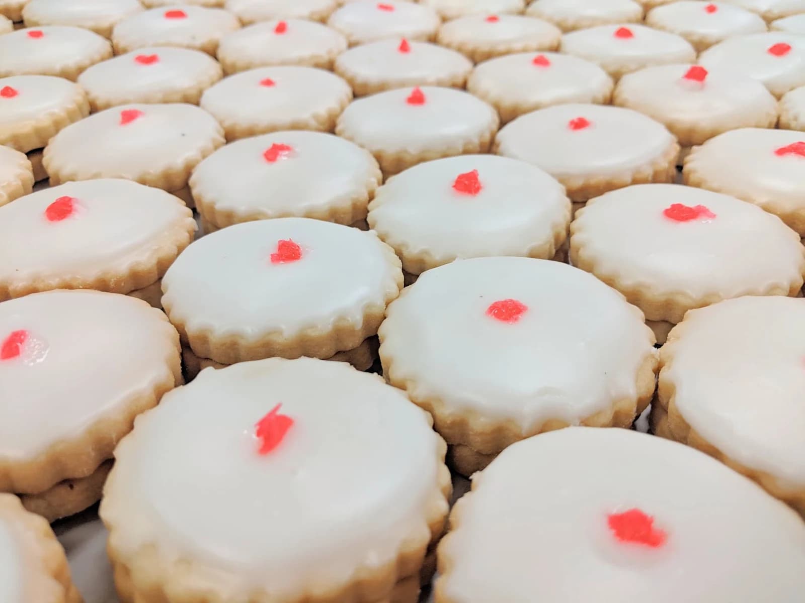 Rows of Empire biscuits with white icing and small red cherry pieces.