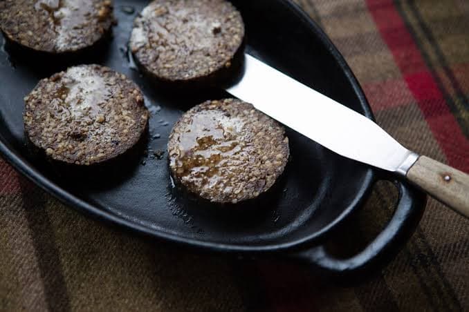 Round slices of haggis on a plate, some pan-fried with a crisp golden crust.