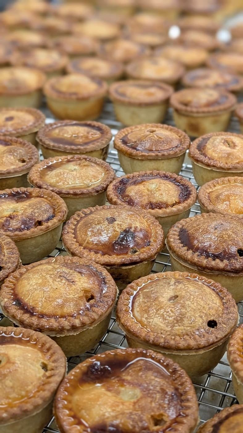 Rows of whole pork pies on bakery racks.