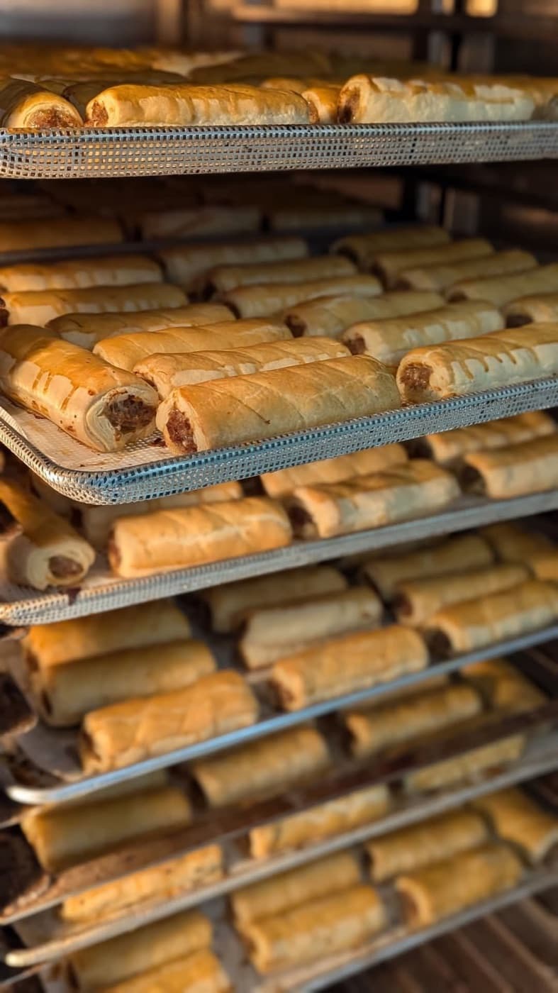 Rows of golden sausage rolls on metal bakery trays.