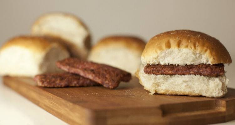 Square sausage served in soft bread rolls on a wooden board.