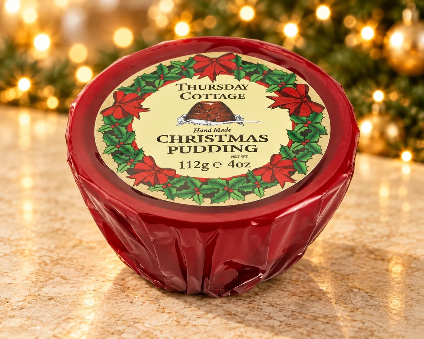 A red-wrapped Thursday Cottage Christmas Pudding with a holly-decorated label.